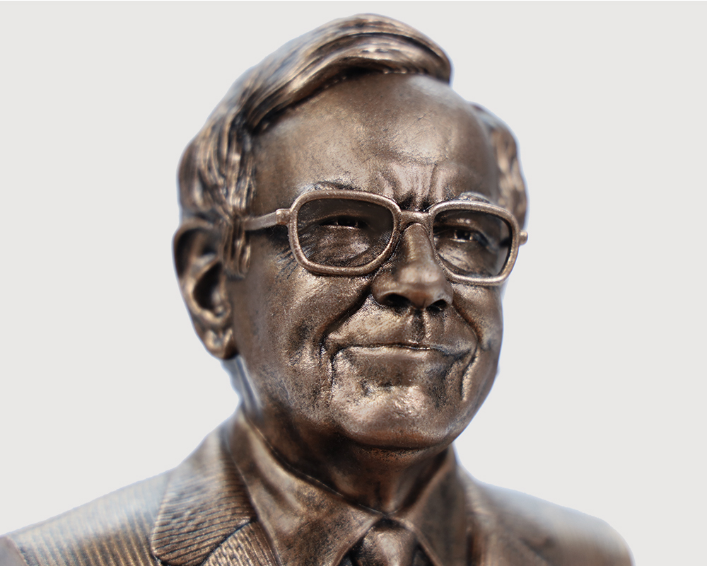 Close-up of bronze Warren Buffett bust statue showing detailed facial features, glasses, and suit texture, photographed from a slight angle on a white background